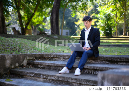 A man from an office sits on outdoor steps using a laptop with a calm and focused work mood A man from an office sits on outdoor steps using a laptop with a calm and focused work mood 134703288