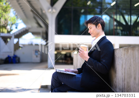 Office man working on laptop outdoors with a coffee cup Office man working on laptop outdoors with a coffee cup 134703331