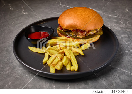 Gourmet burger with fries, ketchup, black plate, appetizing food presentation, delicious meal concept Gourmet burger with fries, ketchup, black plate, appetizing food presentation, delicious meal concept 134703465