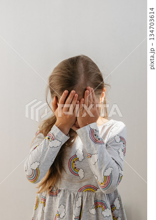 The girl covers her eyes with her hands. The child experiences embarrassment or fear. The girl covers her eyes with her hands. The child experiences embarrassment or fear. 134703614
