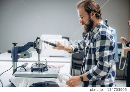 Guy in checkered shirt is working. People are by the sewing machines indoors 134703906