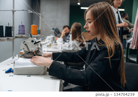 Job of clothing production. People are working by the sewing machines indoors Job of clothing production. People are working by the sewing machines indoors 134704239
