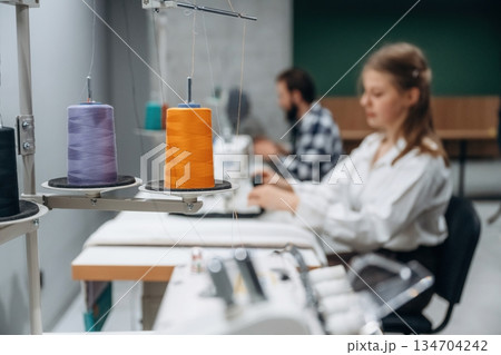View from the side, sitting. People are working by the sewing machines indoors 134704242