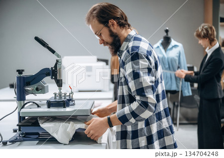 Guy in checkered shirt is working. People are by the sewing machines indoors 134704248