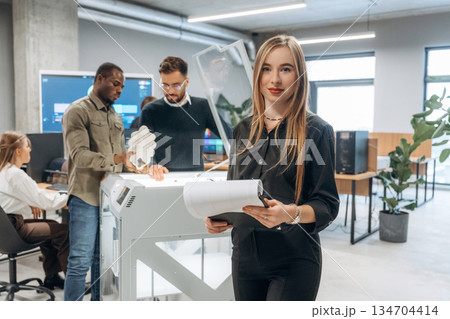 Woman is standing in front of colleagues. People are in the office by the 3d printer Woman is standing in front of colleagues. People are in the office by the 3d printer 134704414