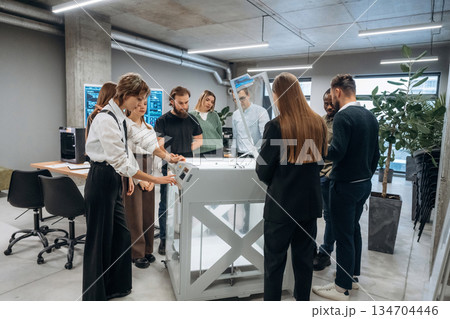 Group of people are standing around the 3d printer in office 134704446