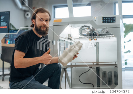 Sitting and holding printed product. Man is in the office with 3d printer Sitting and holding printed product. Man is in the office with 3d printer 134704572