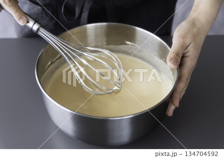泡立て器でケーキ生地を混ぜる手元　ステンレスボウルのクローズアップ 134704592