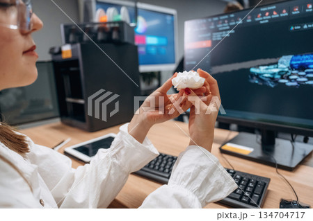 By computer, sitting. Woman is holding 3d printed toy turtle By computer, sitting. Woman is holding 3d printed toy turtle 134704717