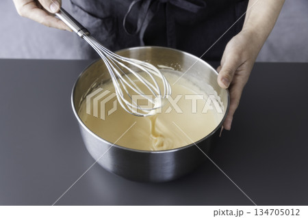 手作りスイーツの下準備　ボウルの生地を泡立て器で混ぜる手 134705012