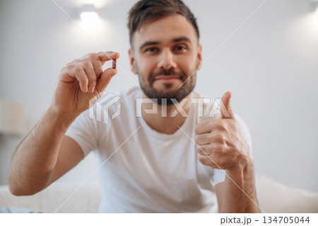 Positive smiling man is sitting holding pill, conception of medicine Positive smiling man is sitting holding pill, conception of medicine 134705044
