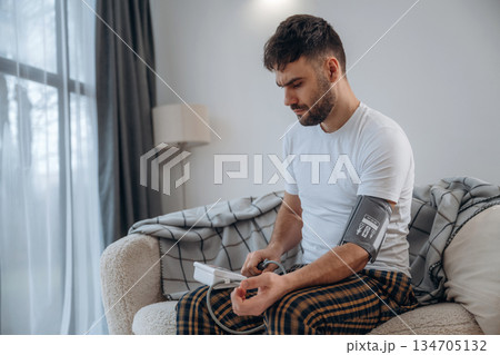 Focused, sitting and measuring blood pressure. Sick man is feeling bad at home Focused, sitting and measuring blood pressure. Sick man is feeling bad at home 134705132