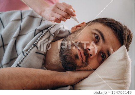 A man lies on a bed. A woman puts ear drops in his ear 134705149