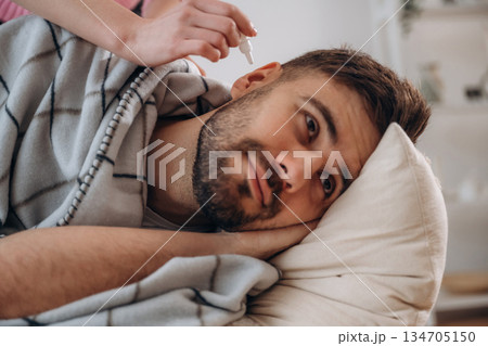 A man lies on a bed. A woman puts ear drops in his ear A man lies on a bed. A woman puts ear drops in his ear 134705150