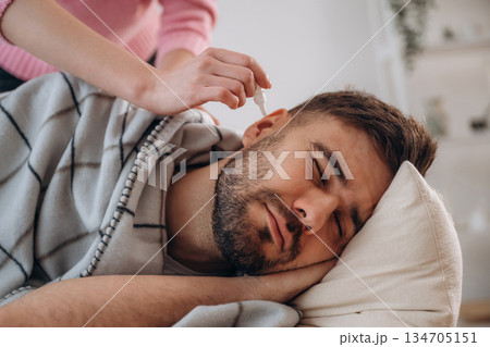 A man lies on a bed. A woman puts ear drops in his ear A man lies on a bed. A woman puts ear drops in his ear 134705151