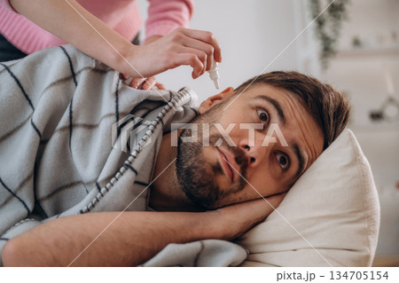 A man lies on a bed. A woman puts ear drops in his ear A man lies on a bed. A woman puts ear drops in his ear 134705154