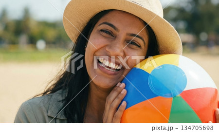 A woman smiles while holding a colorful beach ball at a lively beach in India. It is a sunny day and many visitors are enjoying various activities by the shore. A woman smiles while holding a colorful beach ball at a lively beach in India. It is a sunny day and many visitors are enjoying various activities by the shore. 134705698