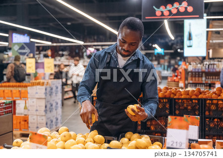 Fresh fruits. Grocery store worker in apron is near products Fresh fruits. Grocery store worker in apron is near products 134705741