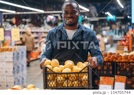 Fresh fruits. Grocery store worker in apron is near products Fresh fruits. Grocery store worker in apron is near products 134705744
