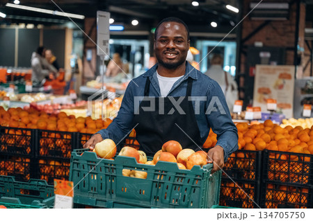 Tasty apples. Grocery store worker in apron is near products Tasty apples. Grocery store worker in apron is near products 134705750