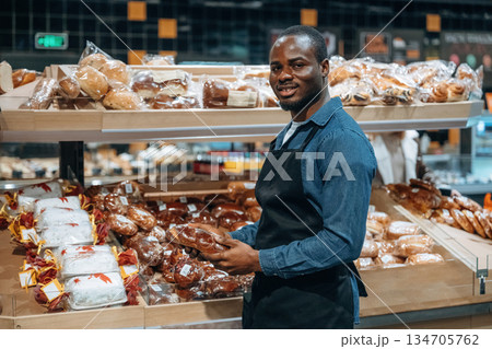 Showing assortment. Supermarket worker is standing near bread products Showing assortment. Supermarket worker is standing near bread products 134705762