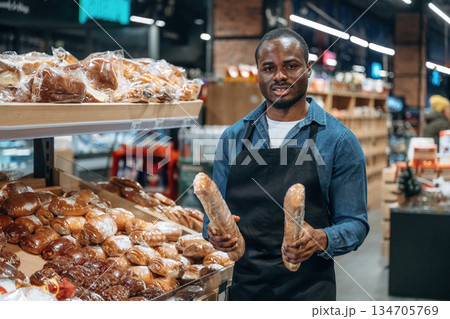 Showing assortment. Supermarket worker is standing near bread products Showing assortment. Supermarket worker is standing near bread products 134705769