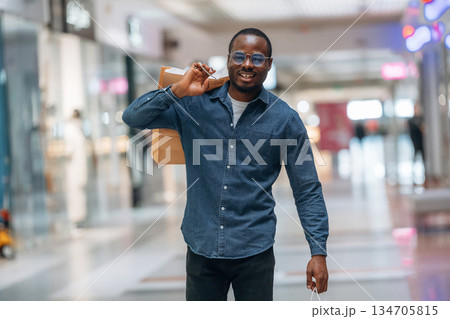 Walking and holding shopping bags. Black man is in the hall of the supermarket Walking and holding shopping bags. Black man is in the hall of the supermarket 134705815