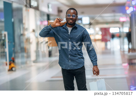 Walking and holding shopping bags. Black man is in the hall of the supermarket Walking and holding shopping bags. Black man is in the hall of the supermarket 134705817
