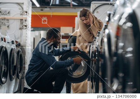 Sitting and opening. Man and woman are choosing washing machine in the store 134706000