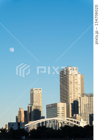 真っ青な青空と昼間の月の下のお台場近くの広々とした東京湾の海面と遠くに見える東京の高層ビル群 134706020