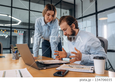 Guy is angry, reading document. Man and woman are in the office together Guy is angry, reading document. Man and woman are in the office together 134706035