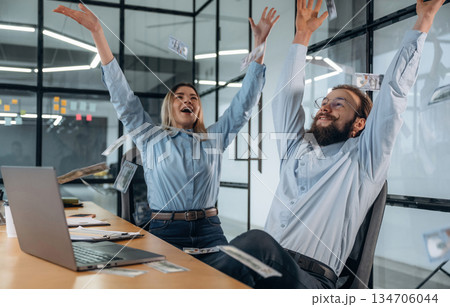 Throwing lot of money up in the air. Man and woman are in the office together Throwing lot of money up in the air. Man and woman are in the office together 134706044