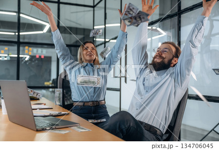 Throwing lot of money up in the air. Man and woman are in the office together Throwing lot of money up in the air. Man and woman are in the office together 134706045