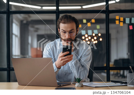 Black smartphone in hands, sitting. Businessman is working in the office Black smartphone in hands, sitting. Businessman is working in the office 134706104