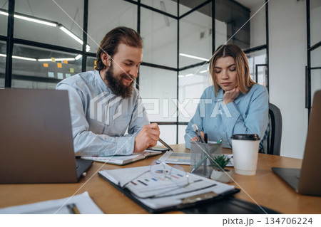 Friendly atmosphere, cup of coffee and laptops. Man and woman are in the office together Friendly atmosphere, cup of coffee and laptops. Man and woman are in the office together 134706224