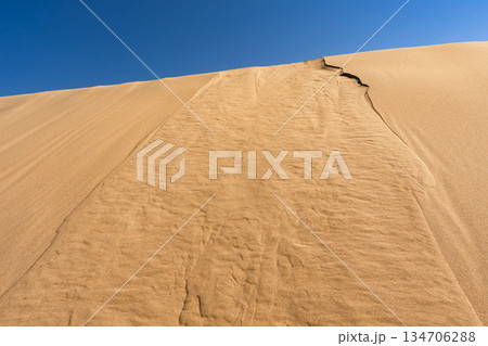 Bottom view of sand dune slope under clear blue sky, textured sand ridges Bottom view of sand dune slope under clear blue sky, textured sand ridges 134706288