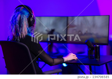 Young female gamer streaming on dual monitors in a colorful gaming setup Young female gamer streaming on dual monitors in a colorful gaming setup 134706585