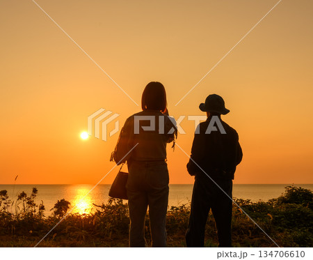 海辺で夕日を見る二人 134706610