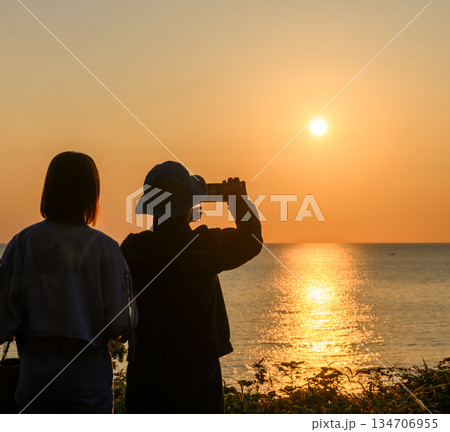 海辺で夕日を撮る二人 134706955
