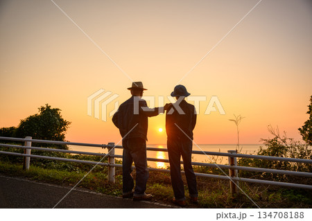 海辺で夕日を見る二人 134708188