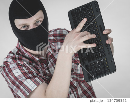 Man wearing balaclava holding keyboard Man wearing balaclava holding keyboard 134709531