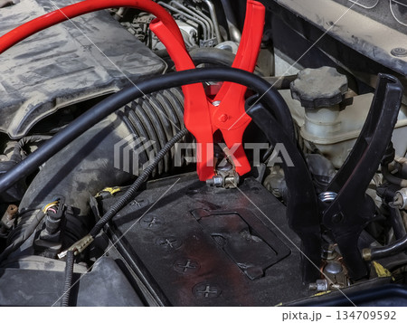 Close-up of car charger cable jump starting a dead car battery. Black and red charging cable clamps on a battery terminals for charging, car repair and maintenance concept. 134709592