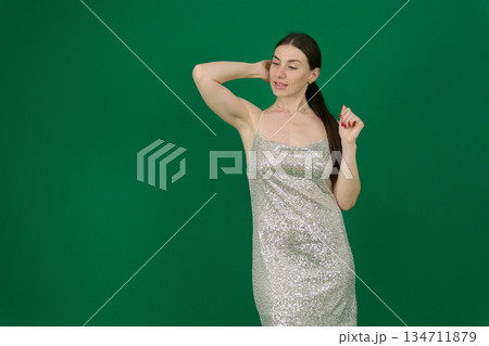 gorgeous woman in a silver shiny dress on a green background chromakey sexuality femininity sensuality . Concept themes of fashion, luxury, elegance, and evening events. gorgeous woman in a silver shiny dress on a green background chromakey sexuality femininity sensuality . Concept themes of fashion, luxury, elegance, and evening events. 134711879