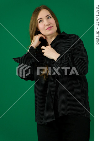 Confident young businesswoman adjusting her hair, exuding professionalism and style in a blue suit against a white background 134711881