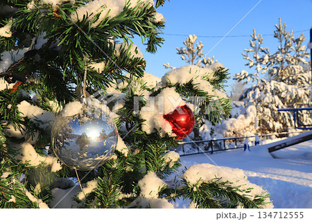 A snow covered Christmas tree outside, decorated for New Year and Christmas. A festive beautiful tree with decorations against a backdrop of live fir trees covered in snow after a snowfall 134712555