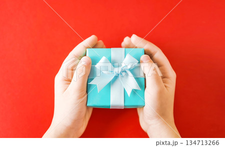 Child's hands holding turquoise gift box on red background Child's hands holding turquoise gift box on red background 134713266