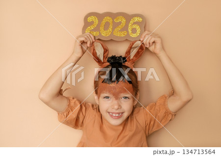 A lovely laughing girl shows the numbers 2026, greeting and congratulating people on the approach of the new year. A child dressed up in a fire horse costume A lovely laughing girl shows the numbers 2026, greeting and congratulating people on the approach of the new year. A child dressed up in a fire horse costume 134713564
