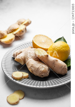 Fresh ginger root and lemon on ceramic plate with leaves on light background. Fresh ginger root and lemon on ceramic plate with leaves on light background. 134713803
