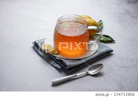 Hot ginger lemon tea in glass cup on a light background with fresh ingredients and spoon. 134713808