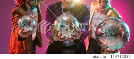 Retro men with disco mirrorballs dancing under neon lights at festive party 134713856